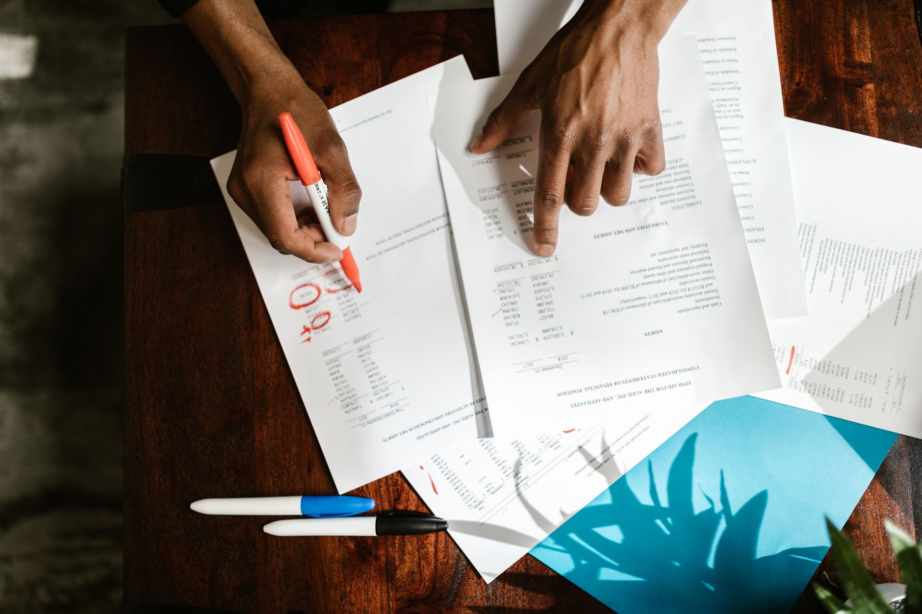 Photo : RDNE Stock project / Pexels Une personne annote au crayon des documents empilés sur un bureau en bois clair